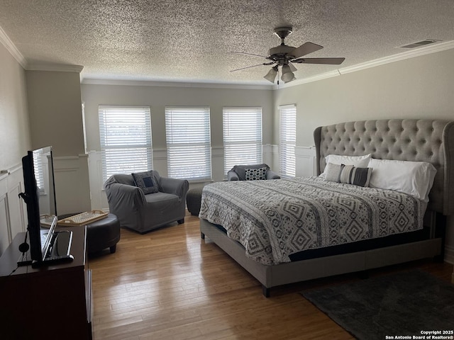 bedroom featuring crown molding, visible vents, wainscoting, a textured ceiling, and light wood-type flooring