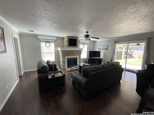 living room featuring visible vents, dark wood-type flooring, ornamental molding, a ceiling fan, and a stone fireplace