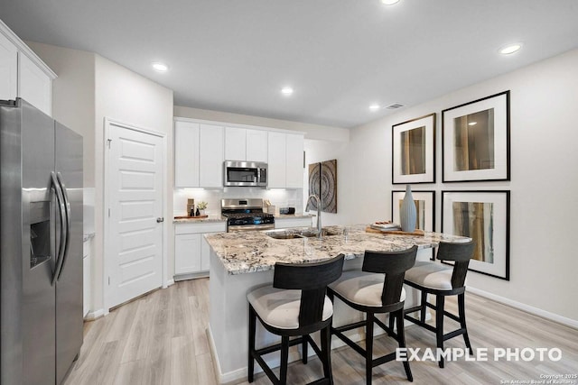 kitchen featuring light wood finished floors, white cabinets, light stone counters, stainless steel appliances, and a sink