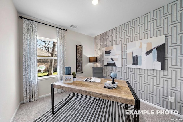 carpeted office with wallpapered walls, baseboards, an accent wall, and visible vents