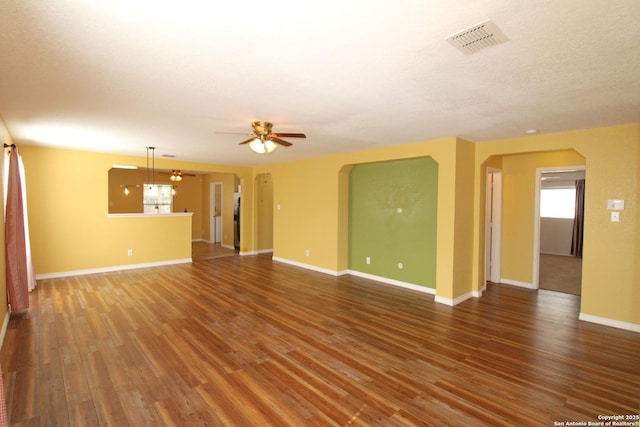 unfurnished living room featuring a ceiling fan, visible vents, baseboards, and wood finished floors