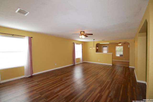 unfurnished living room with a healthy amount of sunlight, baseboards, visible vents, and dark wood-style flooring