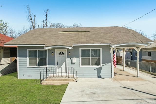 view of front of property featuring an attached carport, a front lawn, roof with shingles, and fence