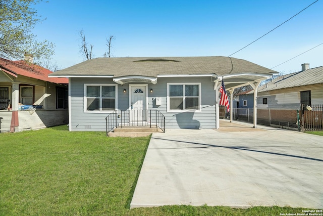 view of front of house with fence, roof with shingles, concrete driveway, a front yard, and a carport