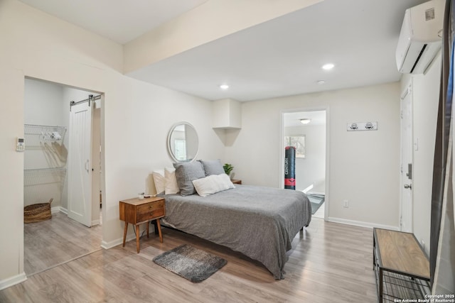 bedroom featuring light wood finished floors, baseboards, a barn door, a wall unit AC, and recessed lighting