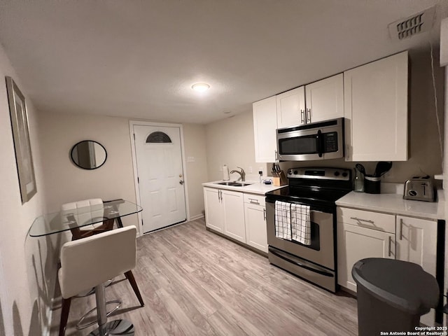 kitchen with a sink, white cabinetry, light wood-style floors, appliances with stainless steel finishes, and light countertops