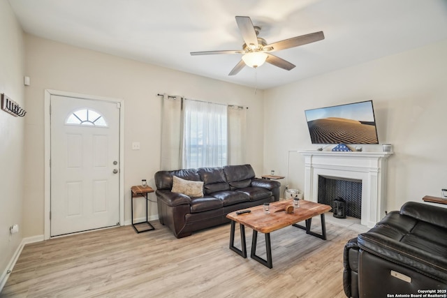 living area with light wood-style flooring, a fireplace with flush hearth, a ceiling fan, and baseboards