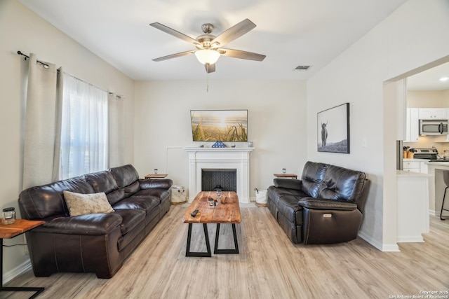 living room featuring visible vents, baseboards, a ceiling fan, and light wood finished floors