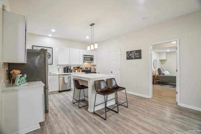 kitchen with a breakfast bar, light wood-style flooring, a center island, stainless steel appliances, and light countertops