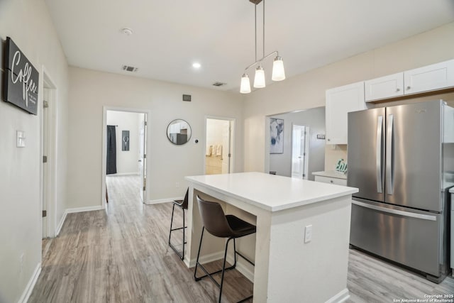 kitchen with visible vents, a center island, freestanding refrigerator, white cabinets, and light countertops