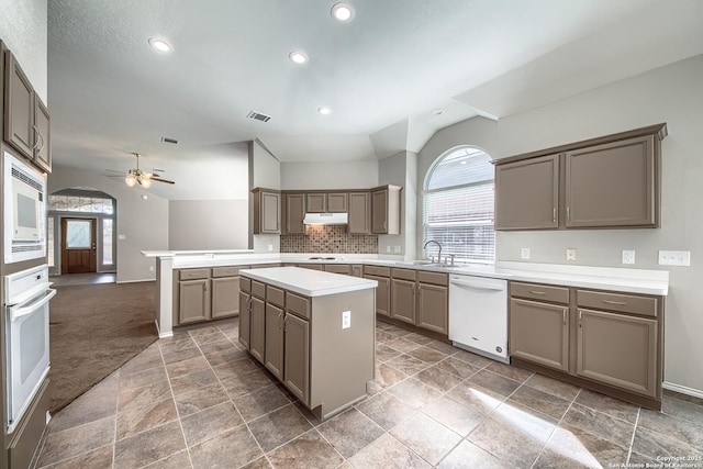 kitchen featuring white appliances, under cabinet range hood, vaulted ceiling, and a sink