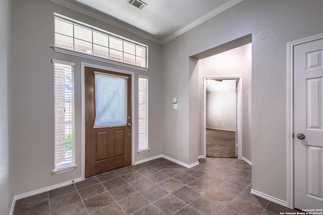 foyer featuring ornamental molding, visible vents, a textured wall, and baseboards