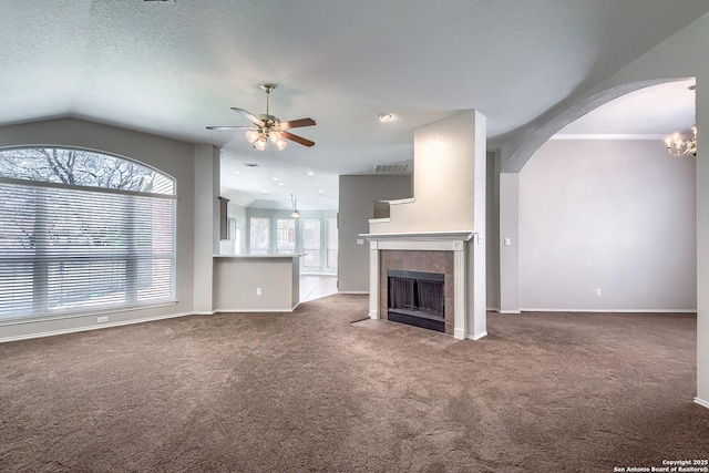 unfurnished living room featuring arched walkways, ceiling fan, a textured ceiling, a fireplace, and carpet