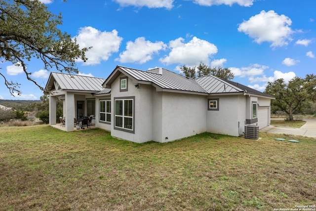 rear view of house with metal roof, an attached garage, a lawn, stucco siding, and a standing seam roof