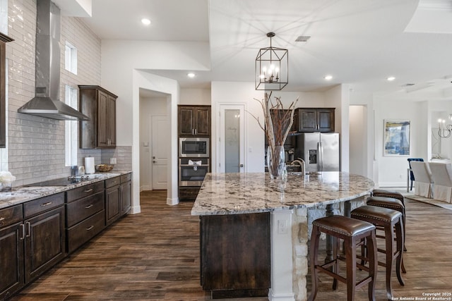 kitchen with dark wood-type flooring, an inviting chandelier, stainless steel appliances, dark brown cabinets, and wall chimney range hood