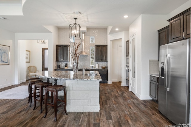 kitchen with light stone counters, stainless steel appliances, dark wood-style flooring, dark brown cabinets, and tasteful backsplash