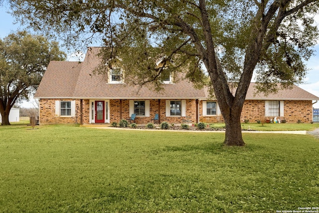 new england style home with a shingled roof, a front yard, and brick siding