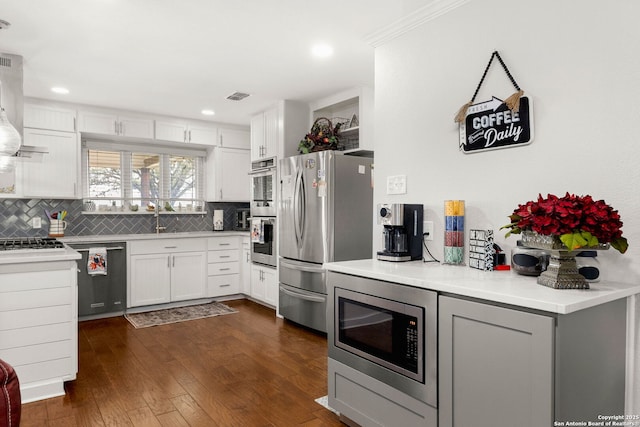 kitchen featuring visible vents, dark wood-type flooring, ventilation hood, stainless steel appliances, and backsplash