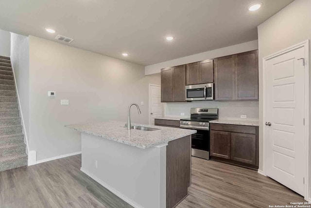 kitchen with stainless steel appliances, visible vents, a sink, an island with sink, and wood finished floors