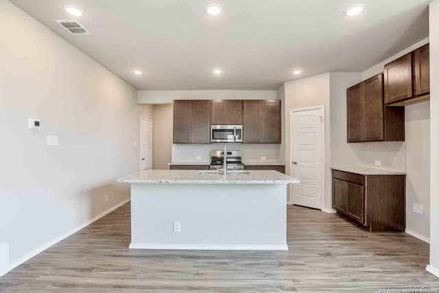 kitchen with a kitchen island with sink, light wood-style flooring, a sink, visible vents, and appliances with stainless steel finishes