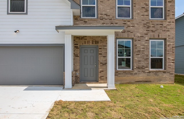 property entrance with a garage, brick siding, and a lawn