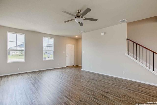 unfurnished room featuring visible vents, a ceiling fan, wood finished floors, baseboards, and stairs