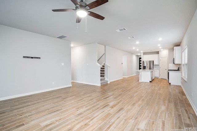 unfurnished living room with visible vents, light wood-style flooring, and stairs