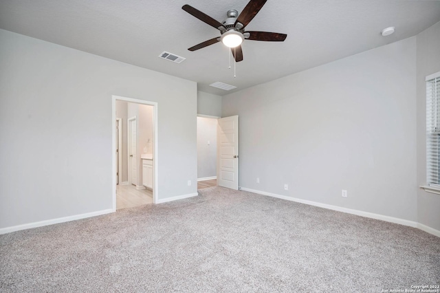 unfurnished bedroom with baseboards, visible vents, connected bathroom, light colored carpet, and ceiling fan