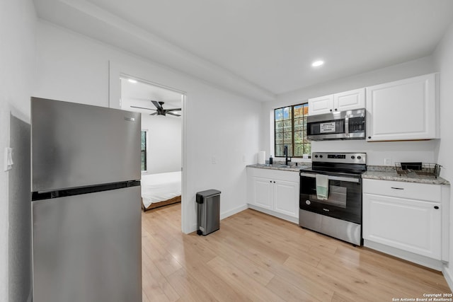 kitchen with stainless steel appliances, light wood-style floors, white cabinets, a sink, and light stone countertops