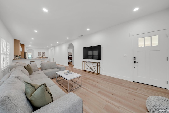 living room with light wood-type flooring, arched walkways, baseboards, and recessed lighting