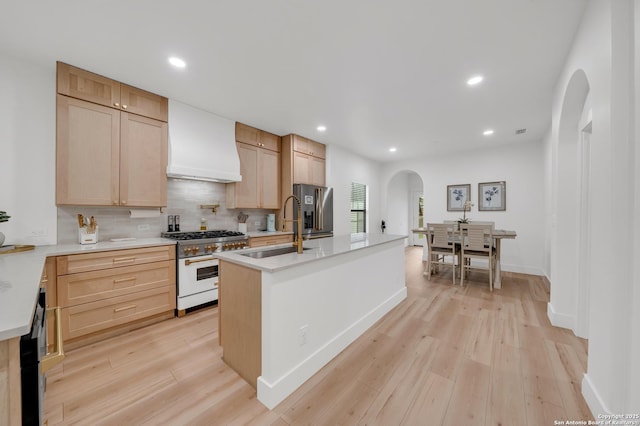 kitchen featuring arched walkways, a sink, custom exhaust hood, range with gas cooktop, and stainless steel fridge