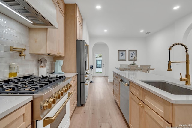 kitchen with arched walkways, a sink, high quality appliances, light brown cabinetry, and custom range hood