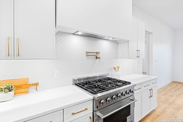 kitchen with light wood finished floors, high end stainless steel range, light countertops, white cabinetry, and backsplash