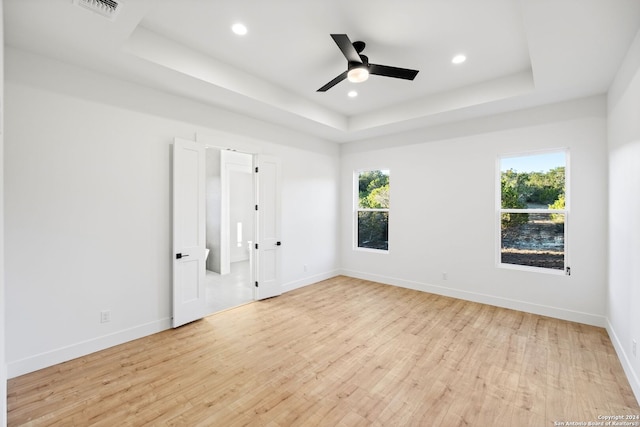 unfurnished room with light wood finished floors, a tray ceiling, visible vents, and baseboards