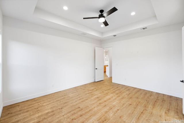 spare room with a tray ceiling, light wood-type flooring, visible vents, and baseboards