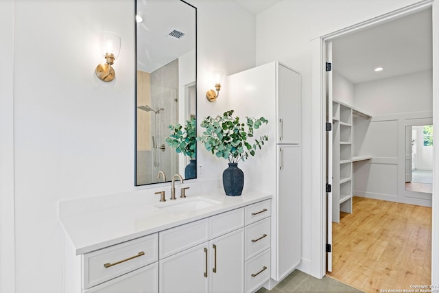 bathroom with wood finished floors, tiled shower, vanity, and visible vents