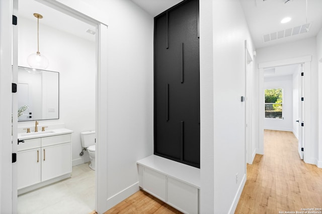 hall featuring light wood-style floors, a sink, visible vents, and baseboards