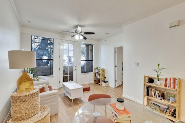 living area with light wood-style floors, baseboards, a ceiling fan, and crown molding