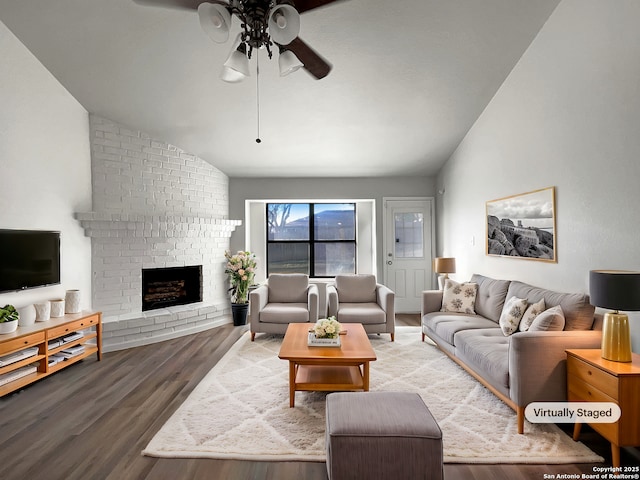 living area with a brick fireplace, ceiling fan, vaulted ceiling, and wood finished floors