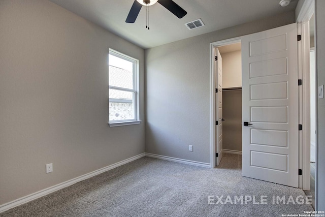 unfurnished bedroom featuring a walk in closet, visible vents, carpet flooring, ceiling fan, and baseboards