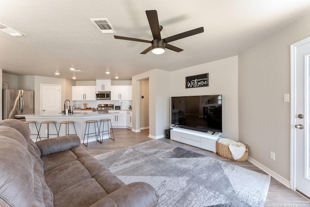 living room with ceiling fan, light wood finished floors, visible vents, and baseboards