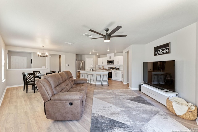 living area with baseboards, visible vents, light wood finished floors, and ceiling fan with notable chandelier