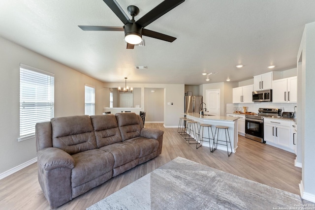 living room with visible vents, light wood-style floors, a textured ceiling, baseboards, and ceiling fan with notable chandelier