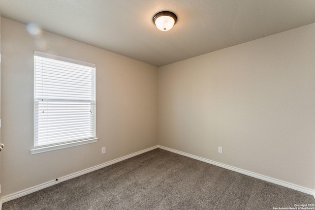 empty room featuring baseboards and dark carpet