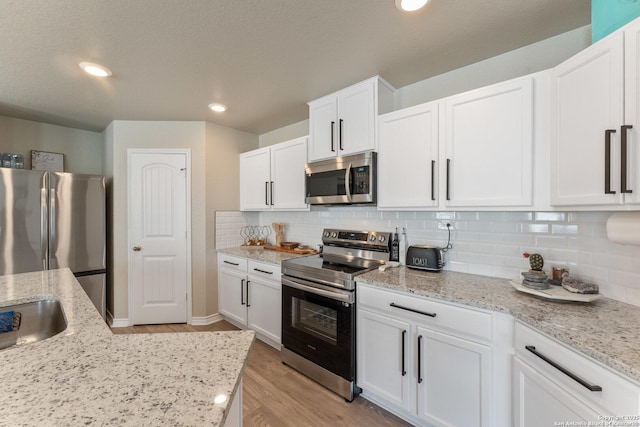 kitchen featuring decorative backsplash, light wood-style flooring, light stone countertops, stainless steel appliances, and white cabinetry