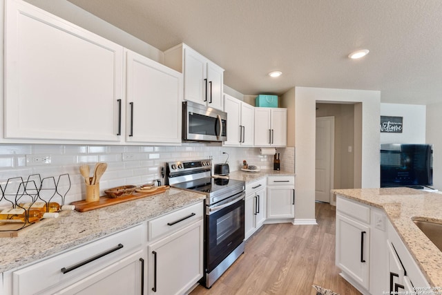 kitchen featuring light wood-style flooring, white cabinetry, stainless steel appliances, and decorative backsplash