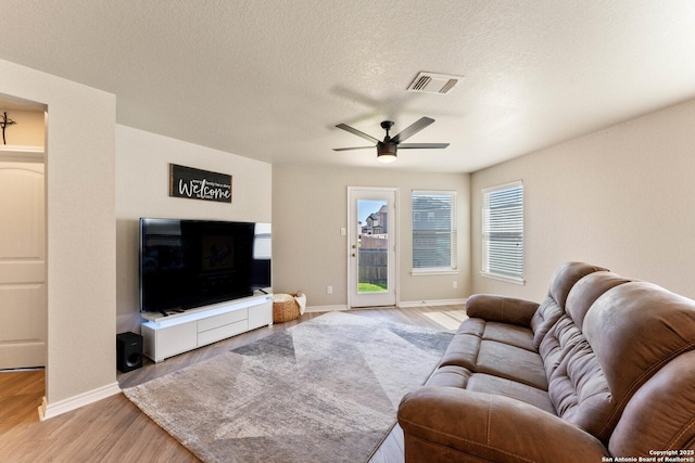 living room featuring visible vents, light wood-style flooring, a ceiling fan, a textured ceiling, and baseboards