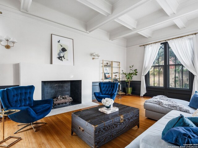 living room featuring a fireplace with flush hearth, a wainscoted wall, beam ceiling, wood finished floors, and coffered ceiling