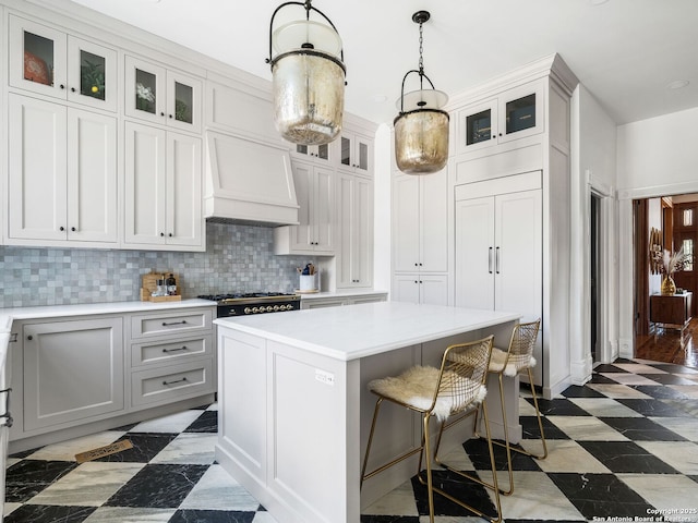 kitchen featuring a center island, a kitchen bar, light countertops, custom range hood, and decorative backsplash