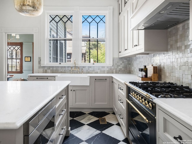 kitchen with a sink, tasteful backsplash, range hood, light countertops, and gas range